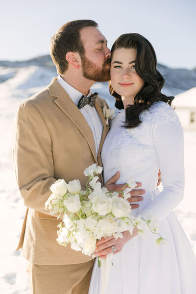 Romantic wedding portrait of bride and groom smiling in the snow holding a white bridal bouquet at The Manor House in Littleton, Colorado