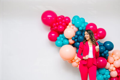 The expertise of Air with Flair, your go-to for premium balloons, decor, and rentals. The expert, dressed in a pink t-shirt and black pants, is crafting a stunning pink and blue balloon installation for the next unforgettable celebration.