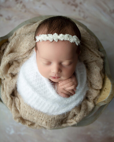 Sleeping newborn girl in white and cream with sweet smile and hands under her chin