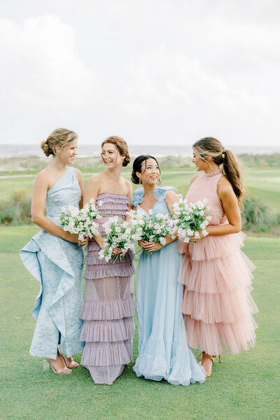 Bridesmaids standing outside in multi color dresses holding white bouquets