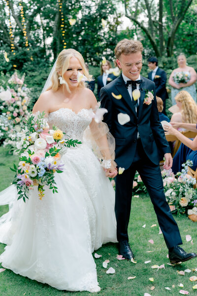 Happy couple walking through colorful petal toss ceremony exit