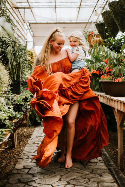 Silken in orange dress holding her daughter in a greenhouse