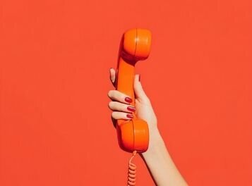 Close-up of a hand holding an orange retro phone, symbolizing reaching out to schedule a free consultation for couples therapy or infidelity recovery with Relationship Experts.