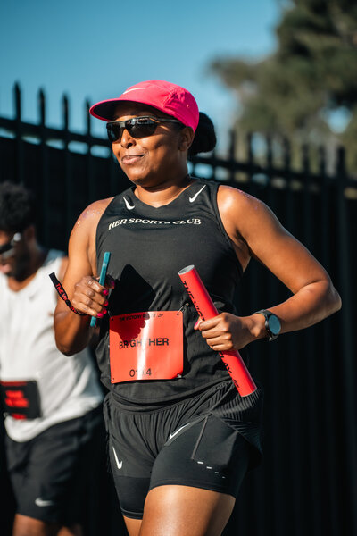 HER Sports Club runner smiling while carrying a baton during a relay session.