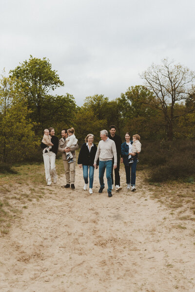 Familie wandelt naar de camera toe over zandpad.