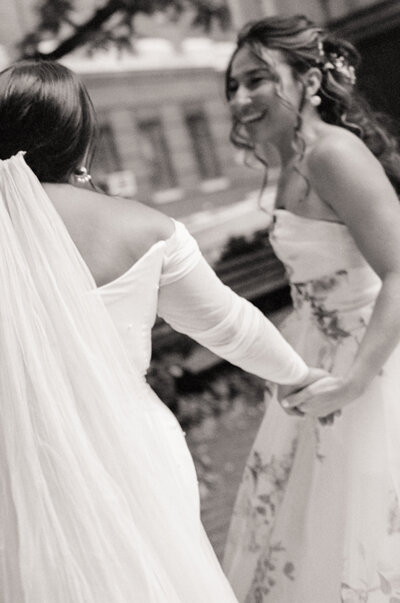 Black and white film photo of two brides holding hands and smiling during their Boston wedding — captured by a film wedding photographer at Castillo Holliday Photo + Film