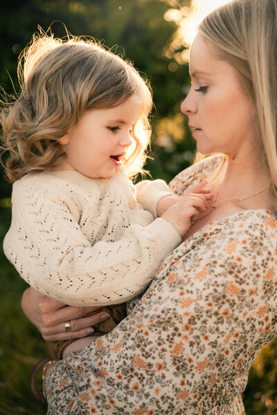 Mum holding daughter whilst they look down at eachother during sunset photoshoot