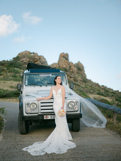 Bride in a chic gown posing with a Land Rover during a luxury destination wedding in St Barth, photographed by Thomas Raboteur