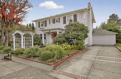 The front of a colonial house with shrubs in the front yard.
