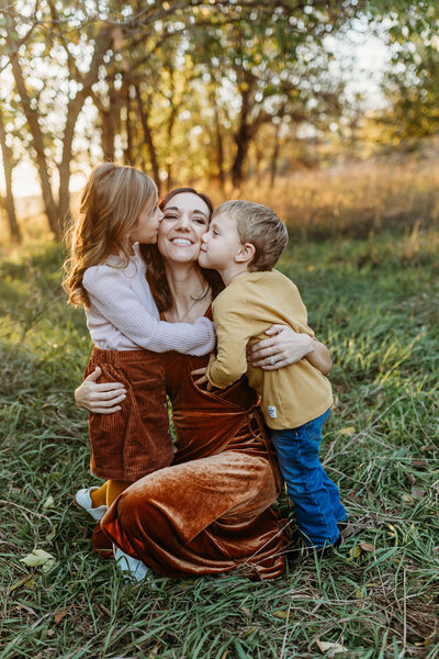 2 kids giving mom kisses in the back field