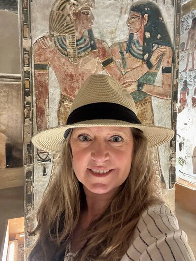Terra Brown from Adventures by Terra inside the tomb of Seti I at Valley of the Kings in Luxor Egypt wearing a straw hat with the colorful tomb carvings behind her