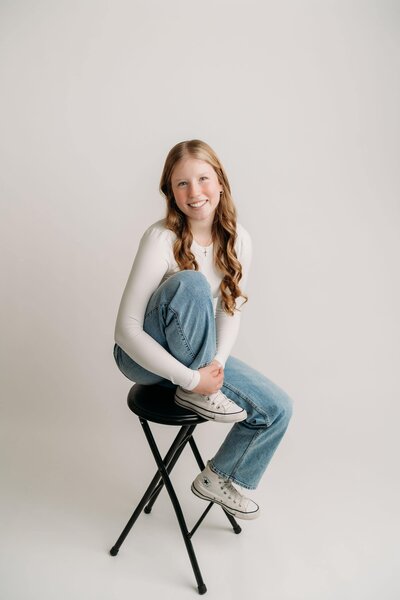 Ava, a website designer, sitting on a chair with one leg bent, looking confidently at the camera during a brand photoshoot