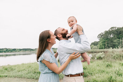 family sitting by lake crabtree park with one year old baby