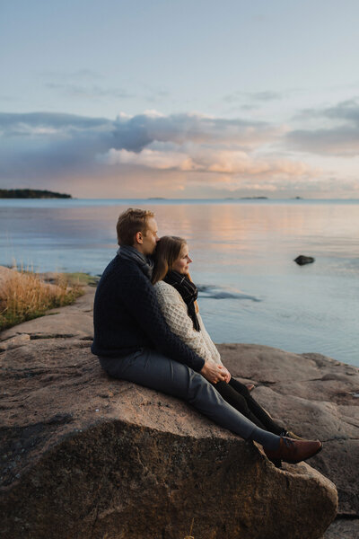 Couple sitting by the sea he hugging her at sunset at fall in Lauttasaari in Helsinki
