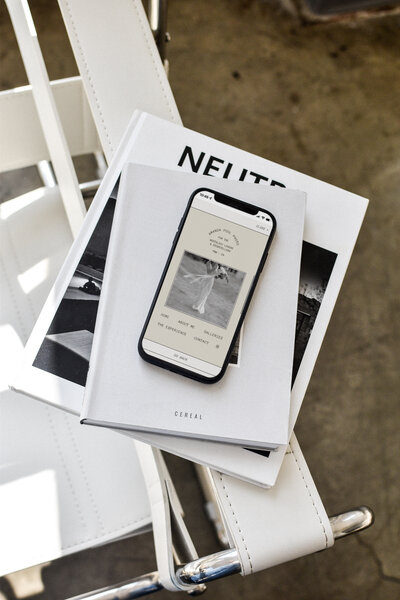 phone with cream and white website open sitting on magazines over a white chair