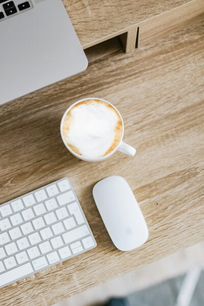 A coffee cup, keyboard, and mouse on a wooden desk.
