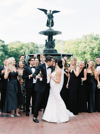 bride and groom kissing after popping champagne with their wedding party