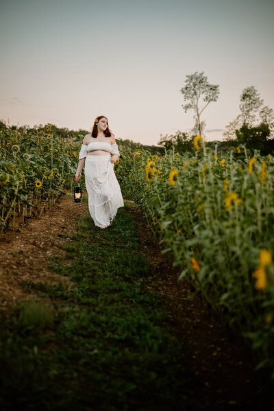 Senior photo of girl walking in sunflower field with lantern look off into the field in Annapolis Maryland.
