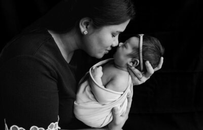 Black-and-white portrait of a mother tenderly holding her newborn baby wrapped in a soft blanket, gently touching noses in a moment of love and connection.