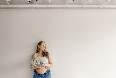 Denver mom holding flowers against her baby bump posing during her pregnancy phtoshoot