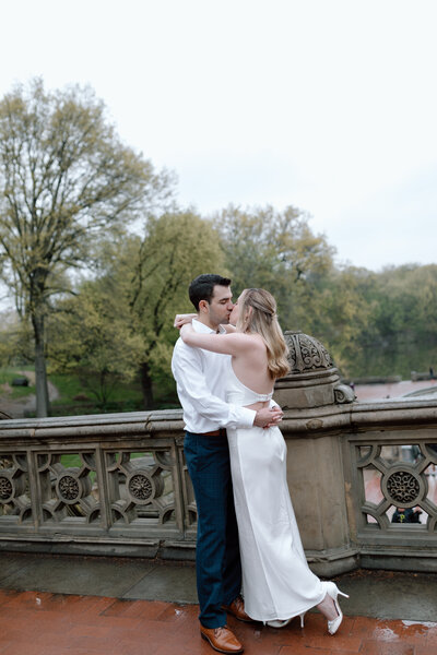 Engaged couple embracing in Central Park, NYC, with lush greenery background, by Hallie Noel Photography.