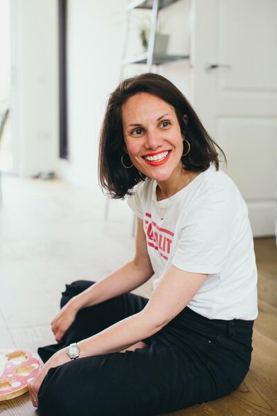 Kaya sitting on the floor smiling brightly, wearing a white T-shirt with red lettering.