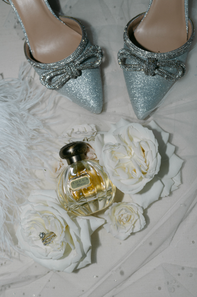 Flat lay of sparkly shoes, perfume, and flowers.