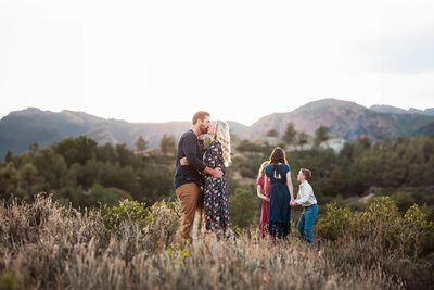 Family poses in their front yard by tall pine trees