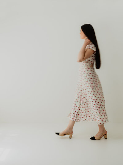 woman in a dress walks across a white backdrop