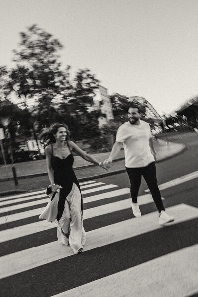 Candid moment of couple walking across a street holding hands captured in black and white by Sunshine Coast photographer