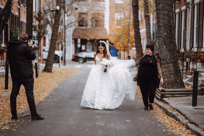 Kristen Catoe helps hold the train of a bride's dress as she walks along a neighborhood street in downtown Philadelphia