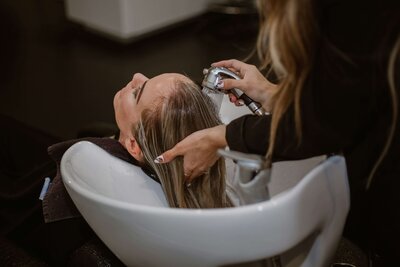 A client receiving a relaxing hair wash at a salon sink, with a stylist gently rinsing their hair, showcasing the soothing and professional service at 212 Salon, Spa, & Barbershop.