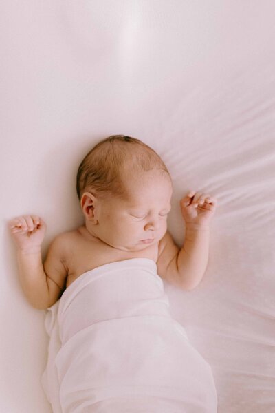 Sleeping baby swaddled in a white swaddle on a white backdrop