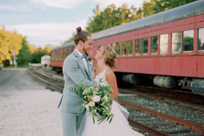 A newlywed couple hugging and smiling at each other in front of a train 