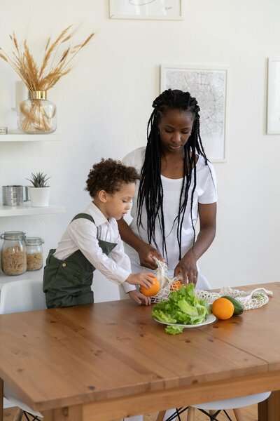 A mom in the kitchen prepping veggies with her toddler. 
