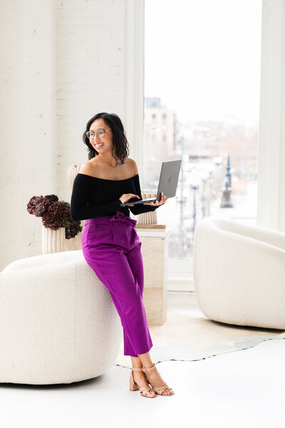 Anh Nguyen, NYC-based photographer, leaning against a chair with a city background.