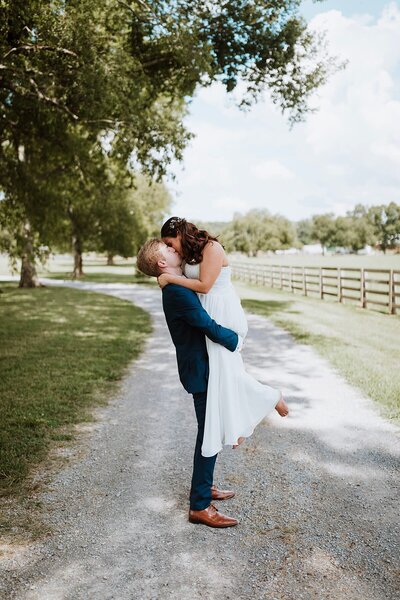 Romantic photo of groom lifting bride and sharing a kiss along a gravel road at Steel Magnolia Barn