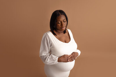 pregnant black woman in cream dress with hands on belly