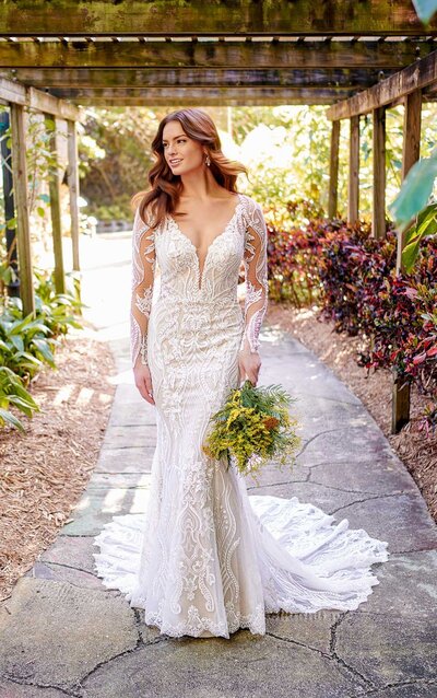 GRAPHIC LACE WEDDING DRESS WITH ILLUSION SLEEVES For a high-end fashion look that is distinctly modern yet evokes a classic romance: meet style D3150. Strong graphic lace details are featured throughout this fit-and-flare silhouette, and are especially prominent as they enwrap the sheer long sleeves for a truly striking focal point. These mixes of scrolling patterns and ornate structures shape and sculpt the figure, from the narrowed plunge of the V-neckline to the sheer cutouts along the sides and back. With a hint of subtle shimmer, the scalloped train features a glitter tulle underlayer for added dimension with every step. A clasp a the top of the back creates a wide keyhole opening, framed with organic floating laces to complete this head-turning look.