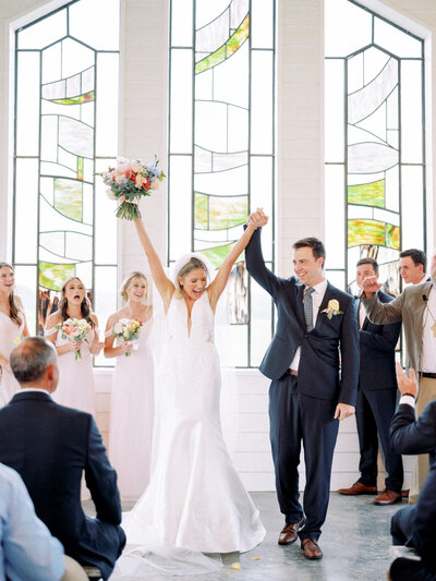 Lindsey Kristian and her husband with their arms raised walking back down the aisle at their wedding ceremony