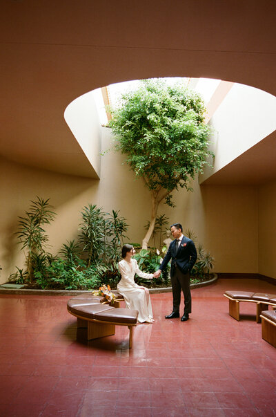 Couple seated beneath skylight and greenery at Civic Center rotunda.