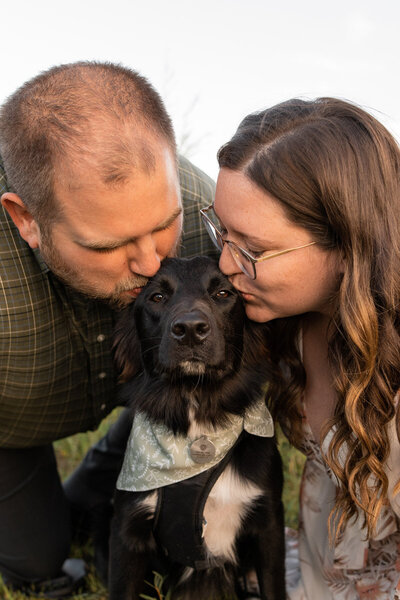 Couple leans in to kiss their dog on the face.