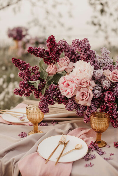 Romantic table setting with pink and purple floral centerpiece and amber glassware