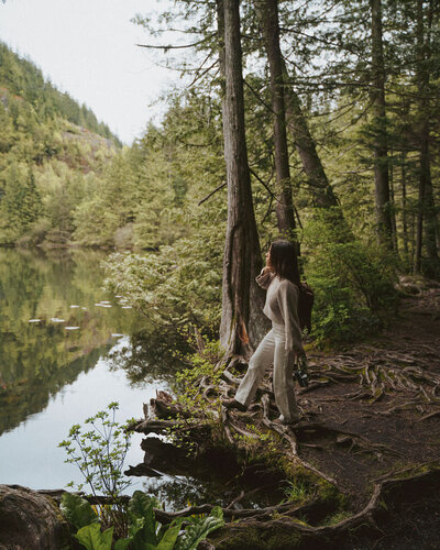 Woman standing in quiet forest by a reflective lake, symbolizing deep inner work, healing, and nervous system regulation through trauma therapy with Jessie Withers in Pasadena