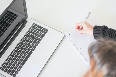 Femme écrivant sur un cahier avec son ordinateur devant elle