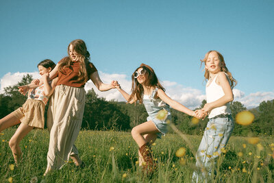 Girls wearing colorful summer outfits holding hands in field at springtime