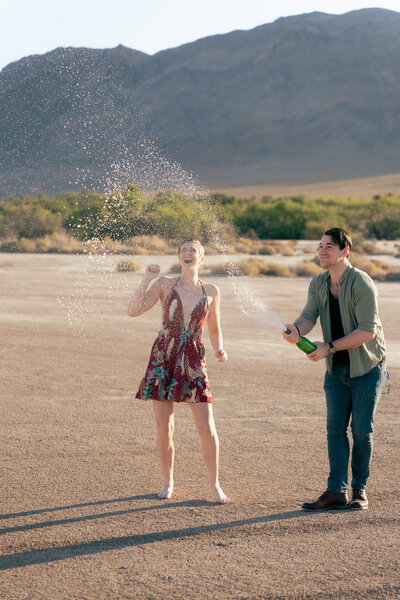 A couple popping a bottle of champagne in the desert