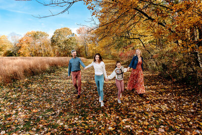 Family holding hands walking through colorful fall foliage captured by Connecticut family photographer during outdoor autumn session