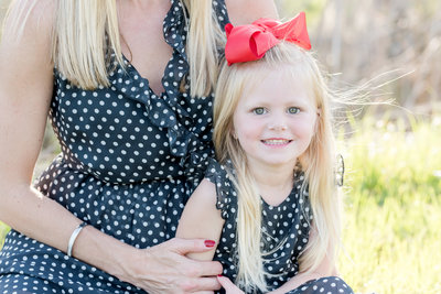 Mother embraces young daughter, both in polka dot dresses
