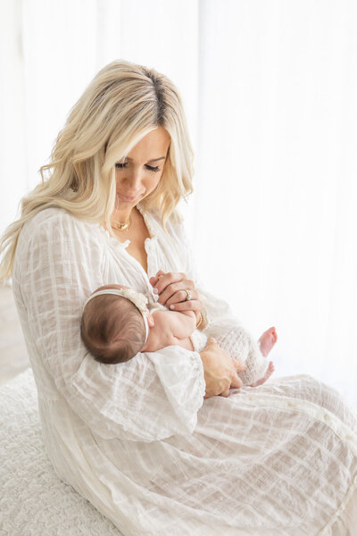 New mom  white dress holding newborn baby girl in a soft light studio. Photographed by newborn photographer One Good Shot Photography in Fresno, CA